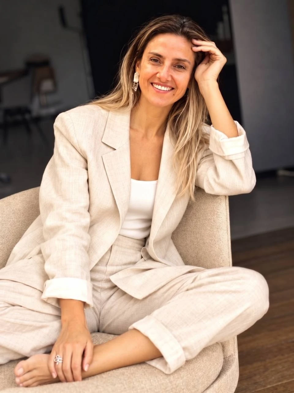 Macarena Landaeta sentada en un sillón, con un conjunto de lino claro.